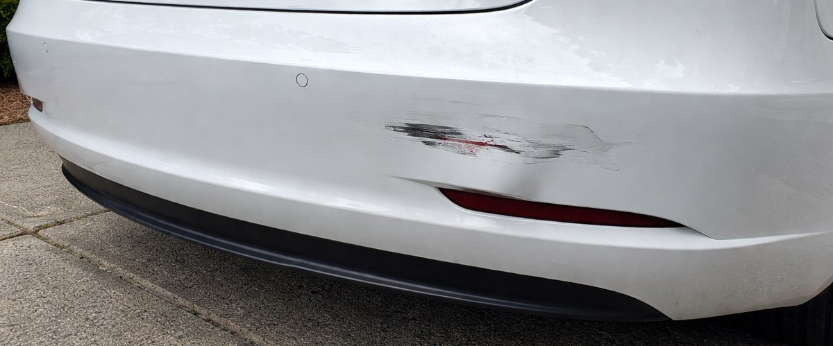 Phone photo of a white Tesla rear bumper with paint transfer and a dent below the reflector